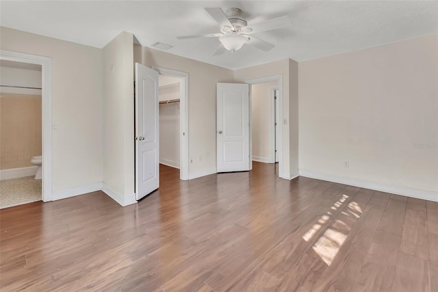 unfurnished bedroom with ensuite bath, ceiling fan, hardwood / wood-style floors, a walk in closet, and a closet