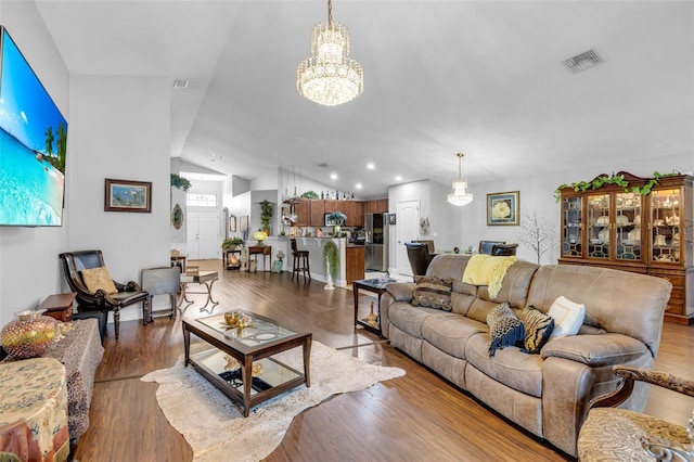 living room featuring an inviting chandelier, vaulted ceiling, and hardwood / wood-style floors