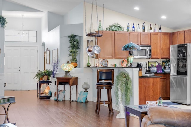 kitchen with wood-type flooring, decorative light fixtures, high vaulted ceiling, appliances with stainless steel finishes, and a notable chandelier