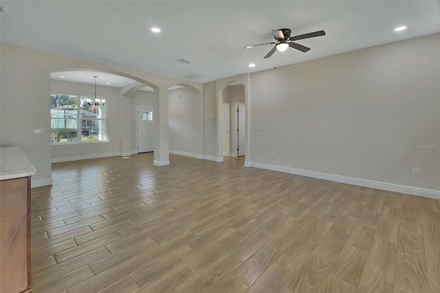 unfurnished living room featuring ceiling fan with notable chandelier and light wood-type flooring