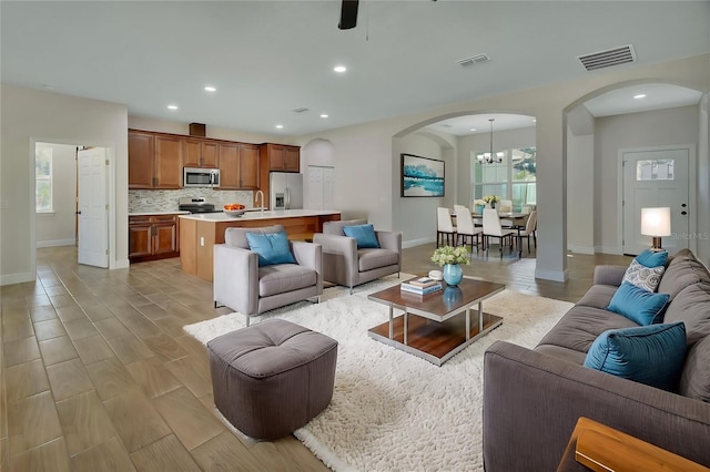 living room with ceiling fan with notable chandelier, sink, a wealth of natural light, and light hardwood / wood-style floors