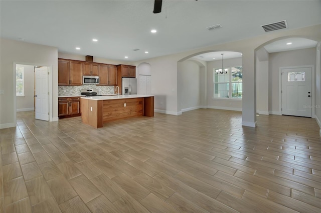 kitchen with light hardwood / wood-style flooring, an island with sink, ceiling fan, stainless steel appliances, and backsplash