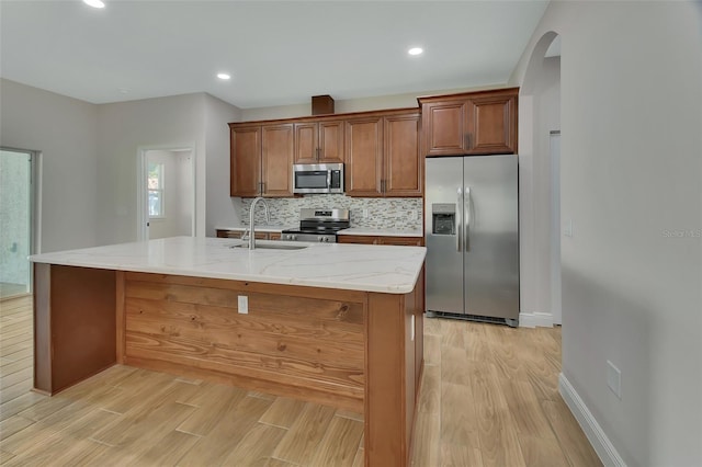 kitchen with stainless steel appliances, sink, a center island with sink, and light hardwood / wood-style flooring