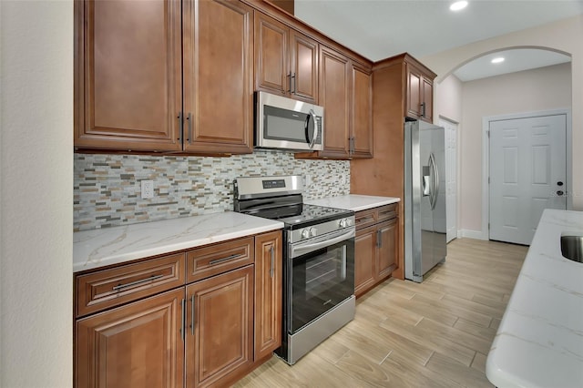 kitchen with light stone countertops, appliances with stainless steel finishes, backsplash, and light hardwood / wood-style flooring