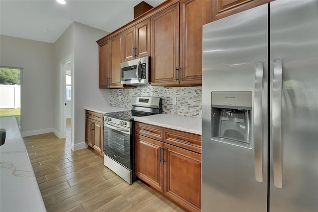 kitchen with appliances with stainless steel finishes, light stone countertops, light wood-type flooring, and backsplash