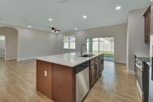 kitchen with sink, a kitchen island with sink, stainless steel dishwasher, ceiling fan, and light stone countertops