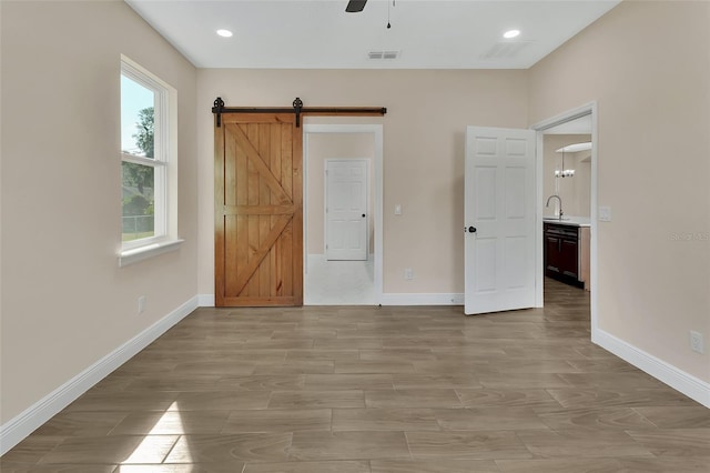 unfurnished bedroom featuring a barn door, sink, and ceiling fan