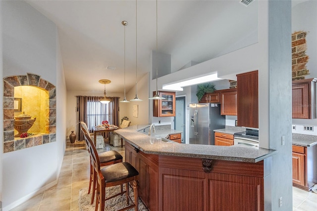 kitchen featuring stainless steel fridge, brown cabinetry, lofted ceiling, a peninsula, and pendant lighting