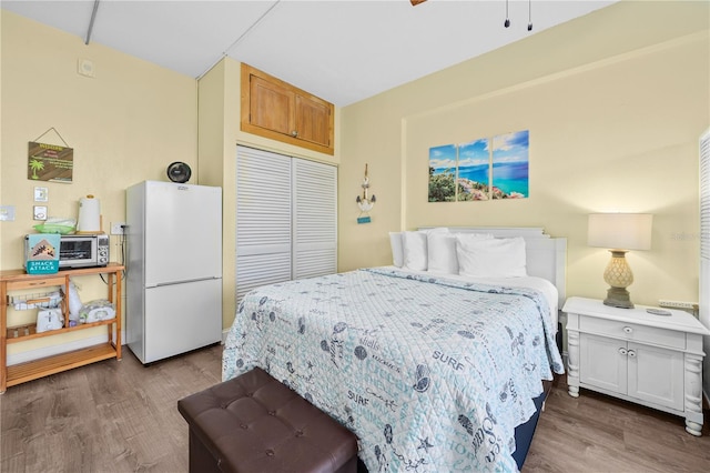 bedroom with a closet, freestanding refrigerator, and wood finished floors