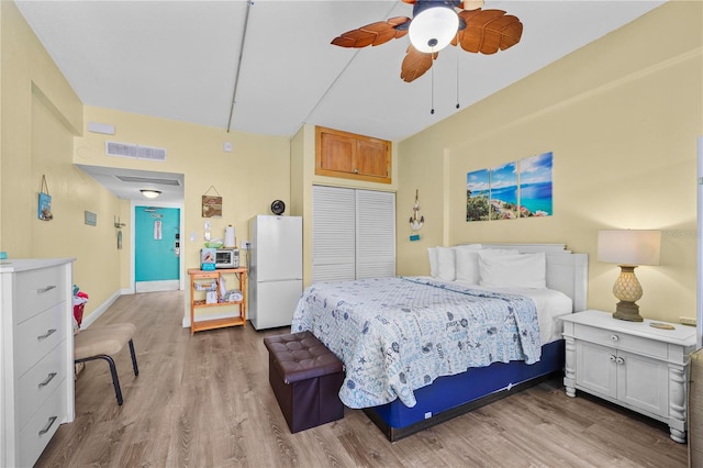 bedroom featuring visible vents, wood finished floors, freestanding refrigerator, a closet, and baseboards