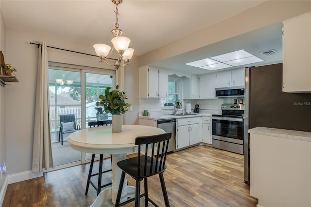 kitchen featuring pendant lighting, backsplash, stainless steel appliances, white cabinets, and light wood-type flooring