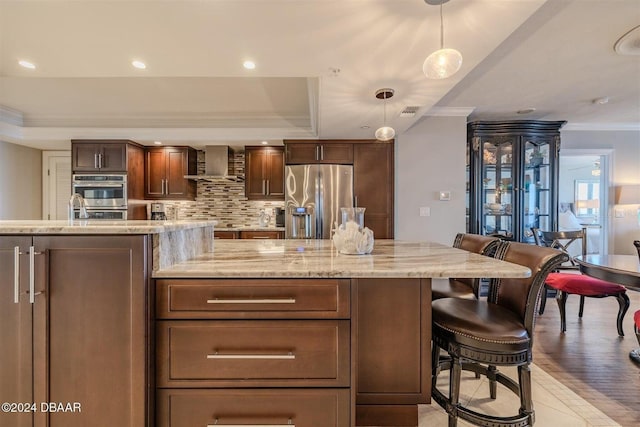 kitchen with wall chimney exhaust hood, hanging light fixtures, a raised ceiling, stainless steel appliances, and decorative backsplash