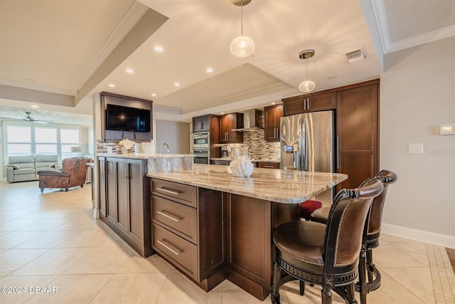 kitchen featuring pendant lighting, a spacious island, light stone counters, stainless steel appliances, and wall chimney exhaust hood