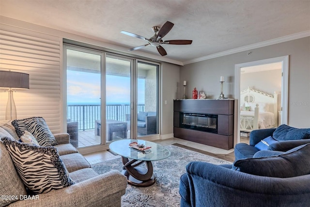 living room with a water view, ceiling fan, ornamental molding, and a textured ceiling