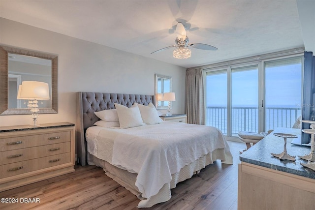 bedroom with wood-type flooring, a water view, access to exterior, and ceiling fan