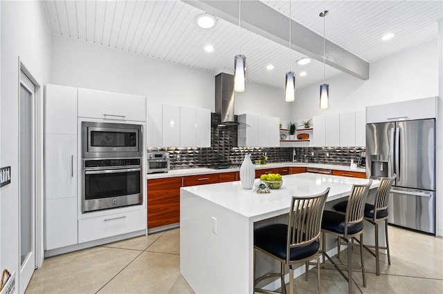 kitchen with white cabinetry, a center island, pendant lighting, stainless steel appliances, and wall chimney range hood