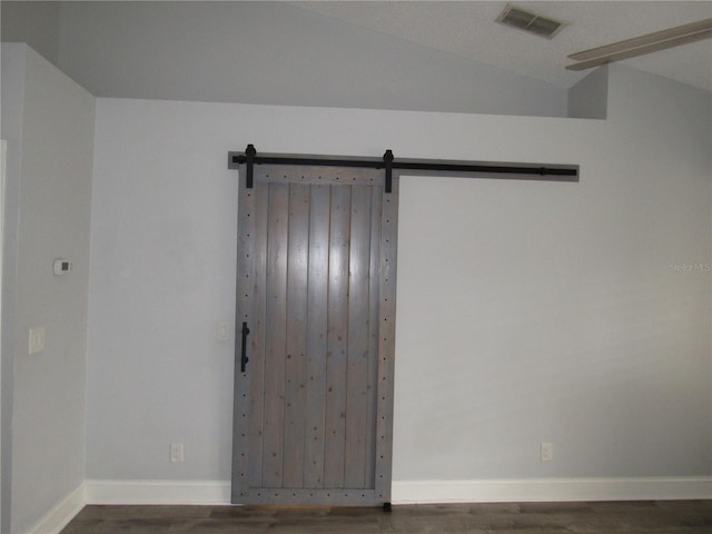 empty room with dark wood-type flooring, lofted ceiling, and a barn door