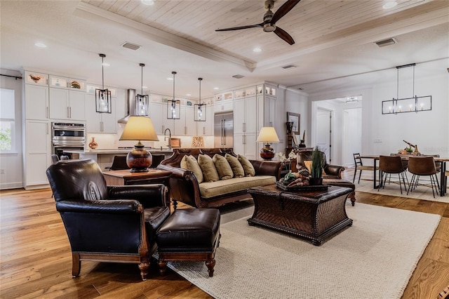 living room with ceiling fan with notable chandelier, a tray ceiling, light wood-type flooring, and wooden ceiling