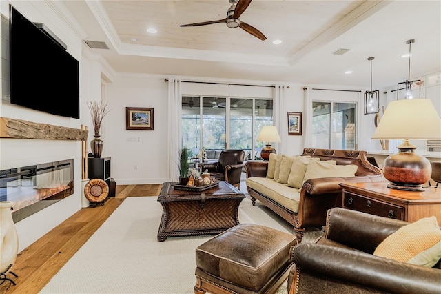 living room featuring ceiling fan, ornamental molding, a raised ceiling, and light hardwood / wood-style flooring