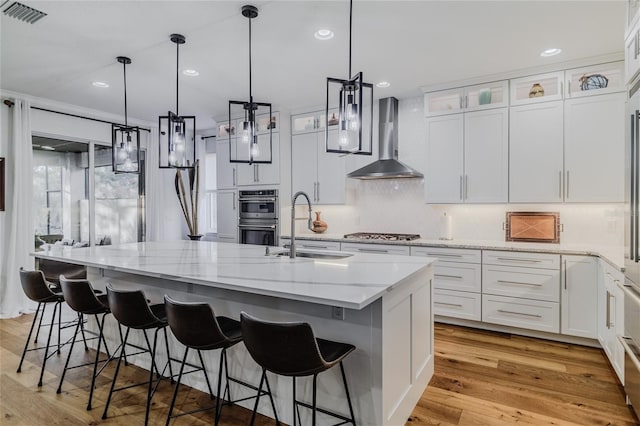 kitchen with white cabinetry, wall chimney exhaust hood, sink, and a kitchen island with sink