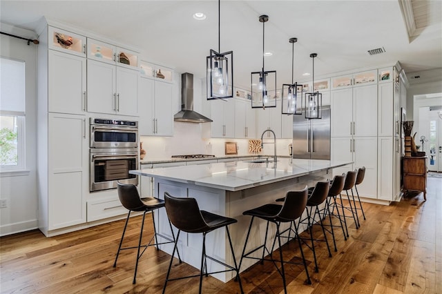 kitchen with a spacious island, wall chimney exhaust hood, sink, appliances with stainless steel finishes, and white cabinets