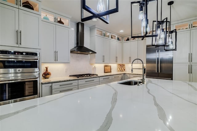 kitchen with appliances with stainless steel finishes, sink, hanging light fixtures, light stone countertops, and wall chimney range hood