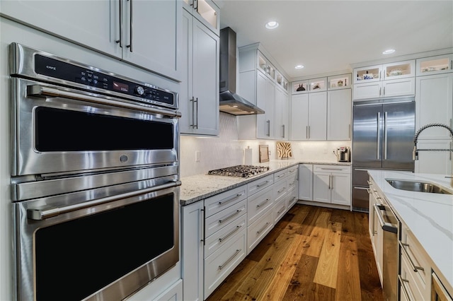 kitchen featuring white cabinetry, wall chimney range hood, stainless steel appliances, and light stone countertops