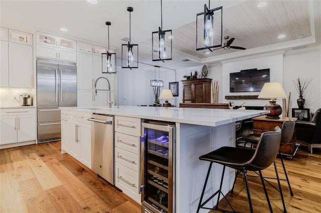 kitchen with decorative light fixtures, beverage cooler, an island with sink, and appliances with stainless steel finishes