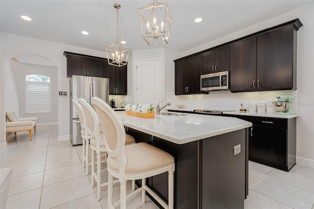 kitchen with appliances with stainless steel finishes, dark brown cabinets, a center island with sink, and sink