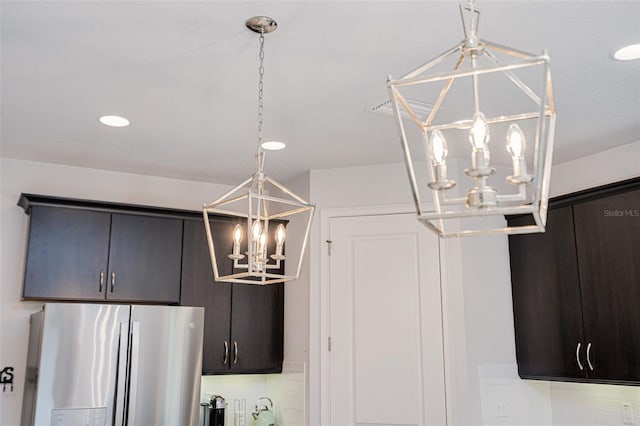 details featuring stainless steel refrigerator with ice dispenser, dark brown cabinets, decorative backsplash, and a notable chandelier