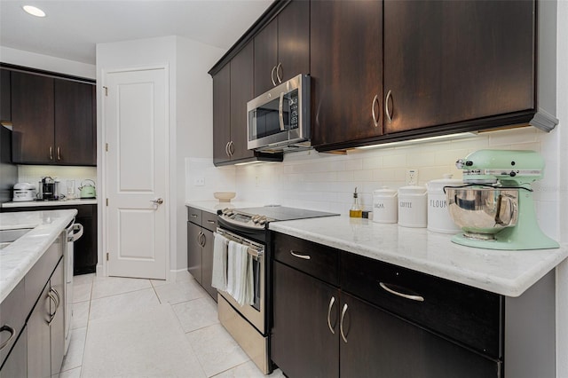 kitchen featuring light tile patterned floors, backsplash, stainless steel appliances, dark brown cabinetry, and light stone counters