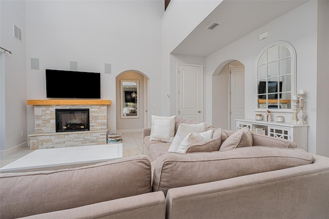 living room with a towering ceiling, a stone fireplace, and light tile patterned floors