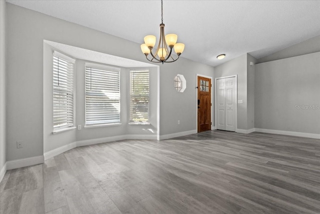 empty room featuring hardwood / wood-style flooring, lofted ceiling, a textured ceiling, and a chandelier