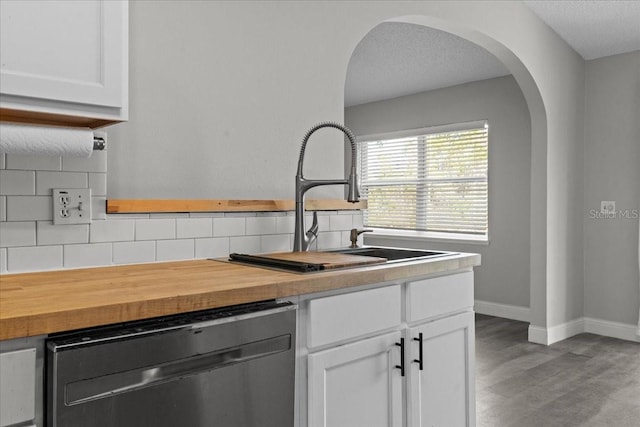 kitchen with sink, white cabinetry, wood-type flooring, decorative backsplash, and stainless steel dishwasher