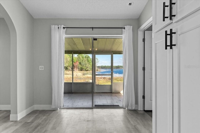 empty room featuring a water view, light hardwood / wood-style floors, and a textured ceiling