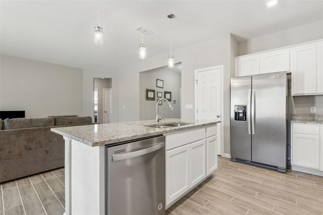 kitchen with pendant lighting, sink, white cabinetry, stainless steel appliances, and a center island with sink