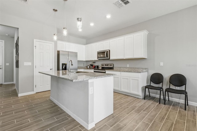 kitchen with white cabinetry, hanging light fixtures, stainless steel appliances, and a center island with sink