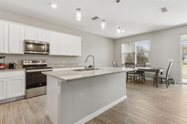 kitchen with appliances with stainless steel finishes, decorative light fixtures, white cabinetry, sink, and a center island with sink