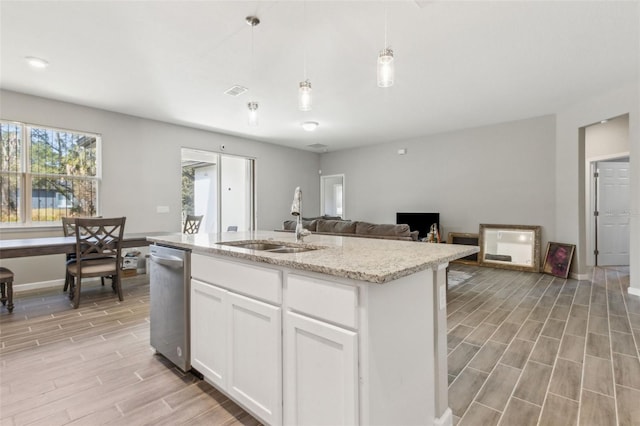 kitchen featuring pendant lighting, an island with sink, sink, white cabinets, and light stone counters