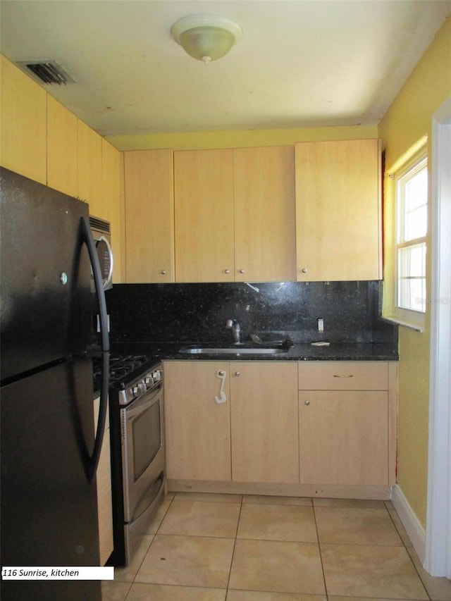 kitchen with appliances with stainless steel finishes, light brown cabinetry, tasteful backsplash, sink, and dark stone countertops