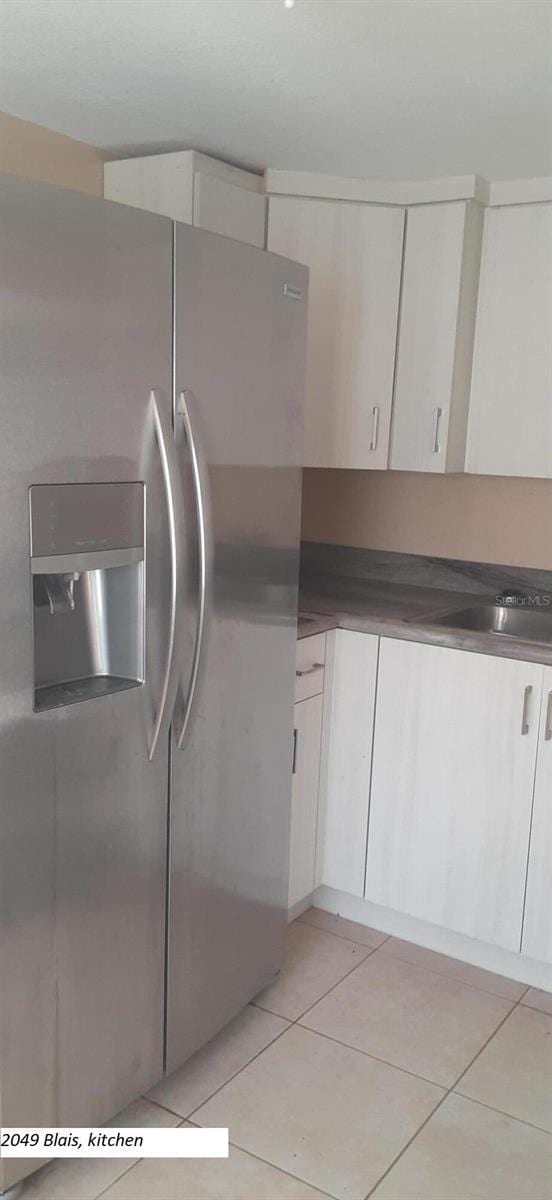 kitchen with stainless steel fridge with ice dispenser, sink, white cabinets, and light tile patterned flooring