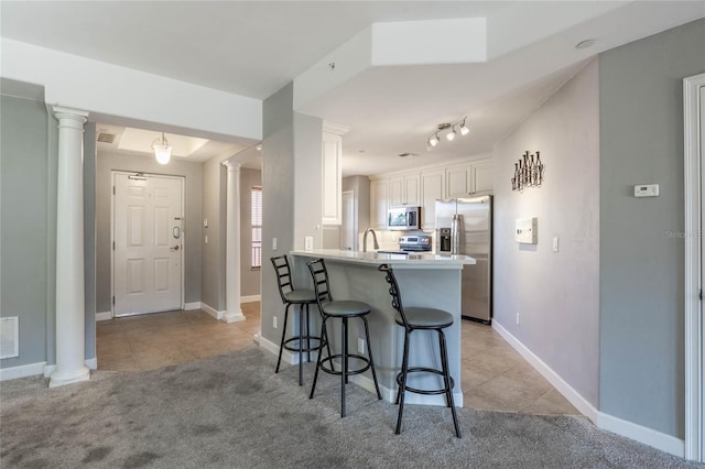 kitchen featuring appliances with stainless steel finishes, decorative columns, a breakfast bar area, white cabinets, and kitchen peninsula