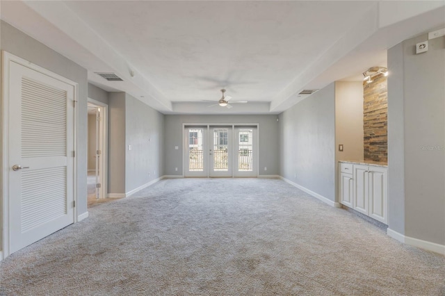 empty room featuring a raised ceiling, light carpet, ceiling fan, and french doors