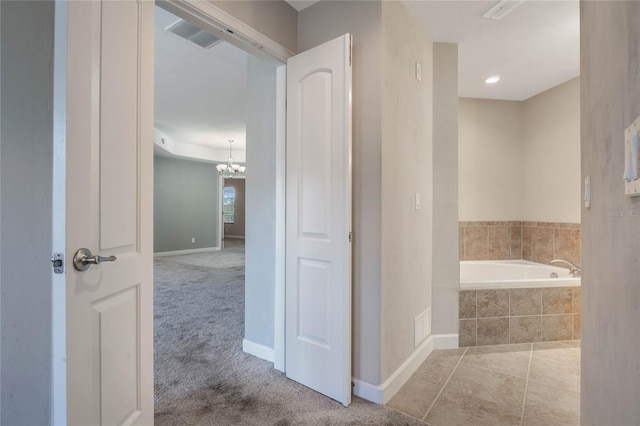 bathroom with a relaxing tiled tub, a notable chandelier, and tile patterned floors