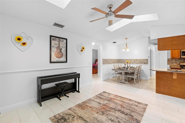 living room with light tile patterned flooring, ceiling fan, lofted ceiling with skylight, and a textured ceiling