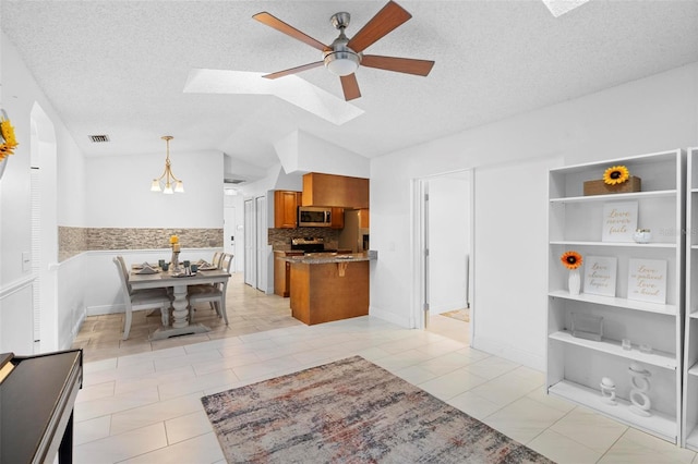 kitchen featuring ceiling fan, appliances with stainless steel finishes, hanging light fixtures, vaulted ceiling with skylight, and kitchen peninsula