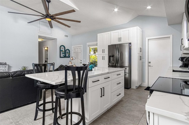 kitchen with lofted ceiling, light stone countertops, white cabinets, and stainless steel fridge with ice dispenser