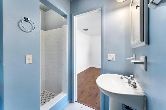 bathroom with tiled shower, wood-type flooring, and sink