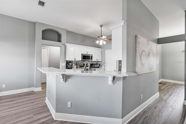 kitchen with a kitchen breakfast bar, stainless steel appliances, white cabinets, decorative backsplash, and kitchen peninsula