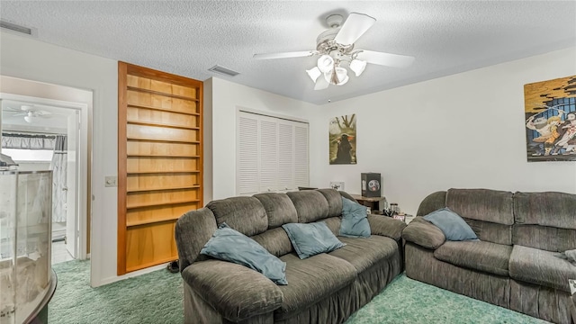 living room with ceiling fan, built in shelves, carpet floors, and a textured ceiling